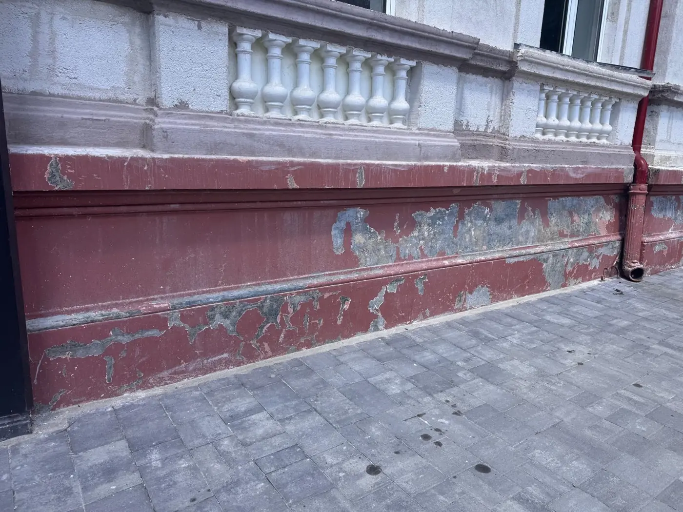 Soclul unei clădiri de patrimoniu, cu vopseaua roșie veche crăpată și exfoliată