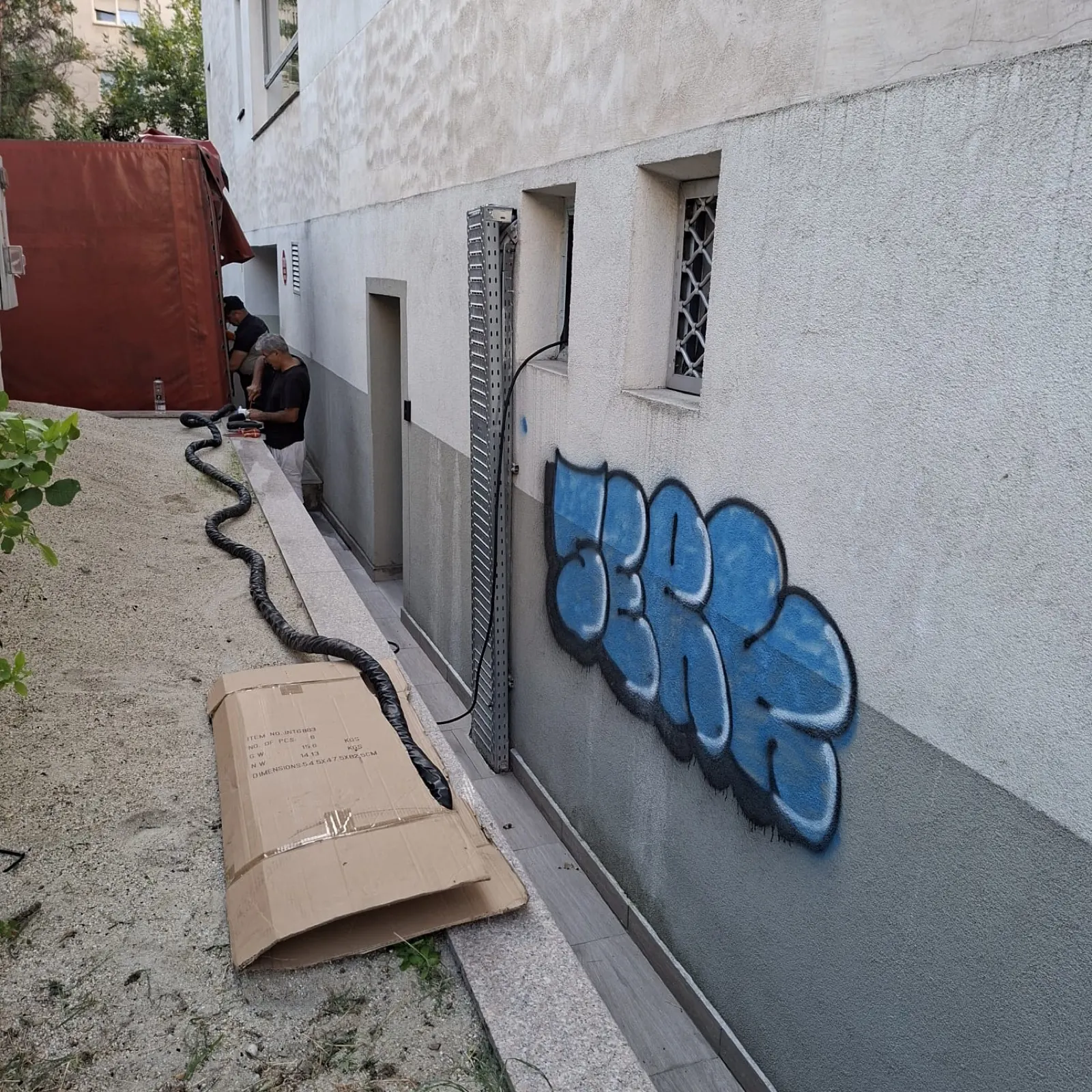 Graffiti proaspăt pe soclul unei clădiri, cu echipamentul laser pregătit alături