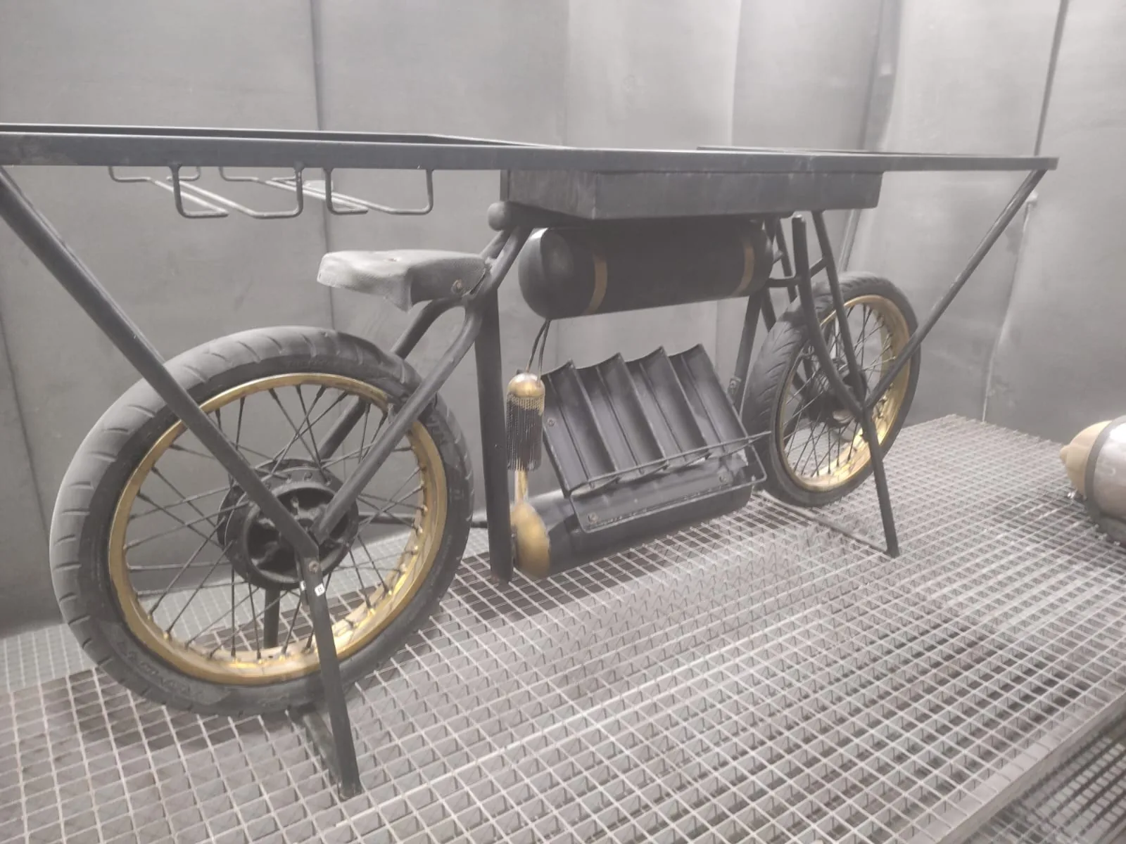 Masă-bar construită dintr-o motocicletă, cu vopseaua neagră tocită și jante aurii, înainte de recondiționare